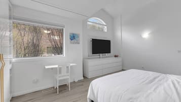 Une chambre à coucher avec un lit, une télévision, un bureau et une fenêtre donnant sur des arbres.