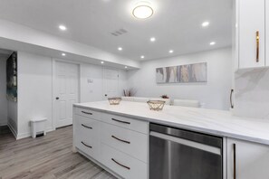A modern kitchen with white cabinetry, a stainless steel dishwasher, and recessed ceiling lighting.