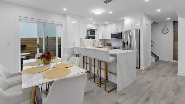 Una cocina moderna con armarios blancos, una isla central y un comedor con sillas y una mesa blancos.
