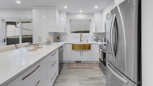 Una cocina moderna con armarios blancos, un refrigerador de acero inoxidable y una isla grande con encimera dorada.