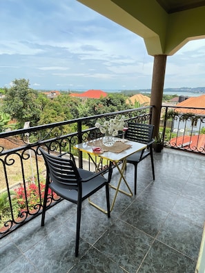 Ein Balkon mit zwei Stühlen und einem Tisch, Blick auf Häuser und Grünflächen, mit Fliesenboden.