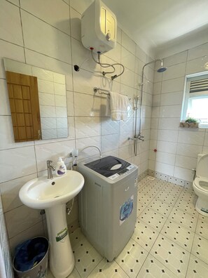 Un bagno con lavandino, lavatrice, porta asciugamani e doccia.