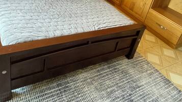 A bed with white linens, a wooden headboard, a nightstand with a lamp, and a wooden wardrobe.