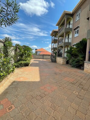 A paved walkway leading to a building with multiple balconies and a red-roofed structure in the background.