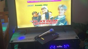 Un écran d’ordinateur affichant la pochette d’un album de musique, un microphone sur un pied et un mur orné de panneaux décoratifs.