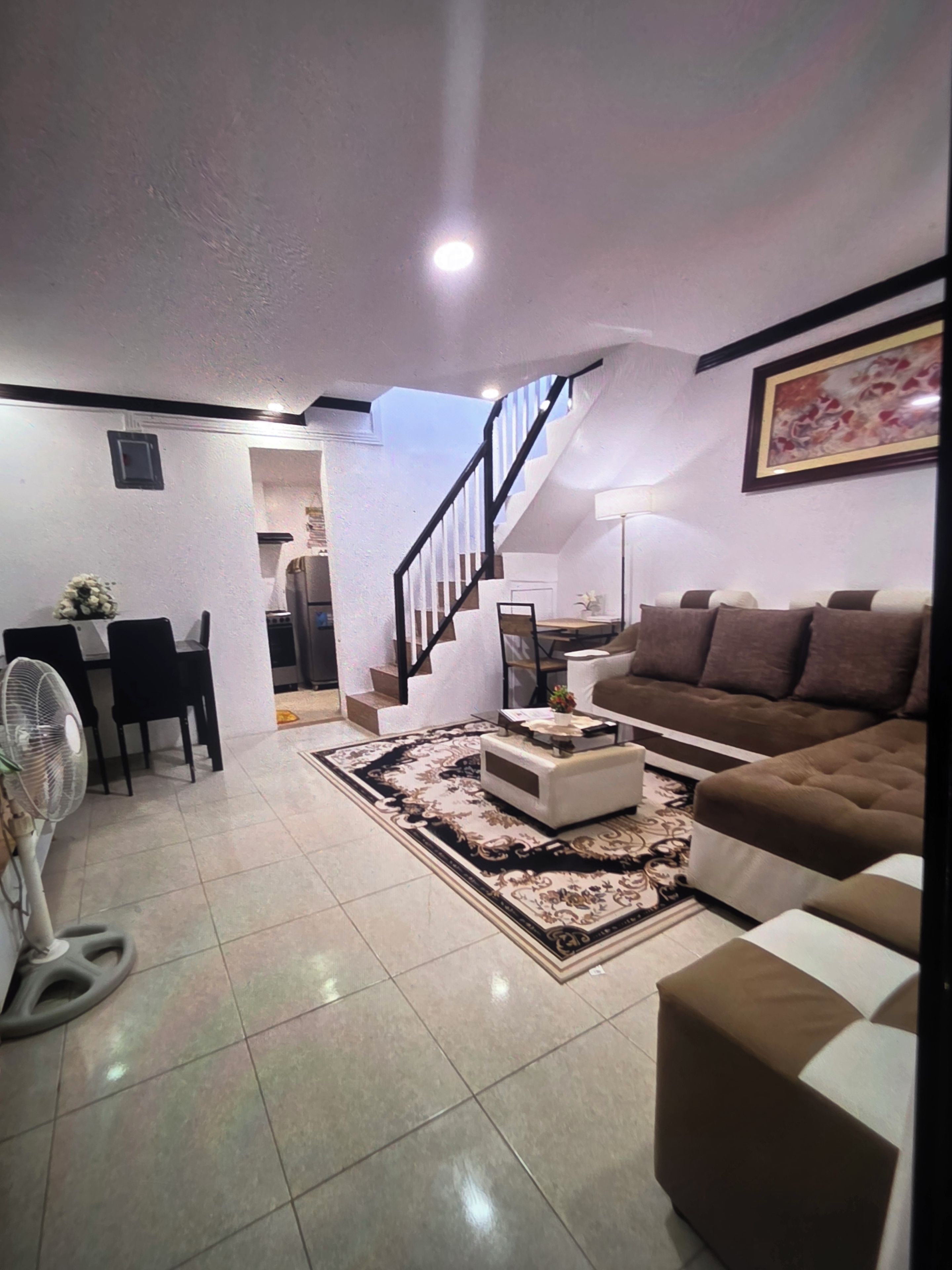 A living room with a sofa, a coffee table, a fan, and a staircase leading to another room.
