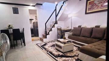 A living room with a sofa, a coffee table, a fan, and a staircase leading to another room.