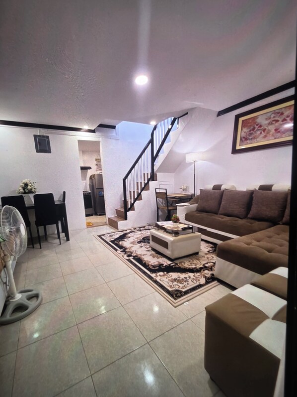 A living room with a sofa, a coffee table, a fan, and a staircase leading to another room.
