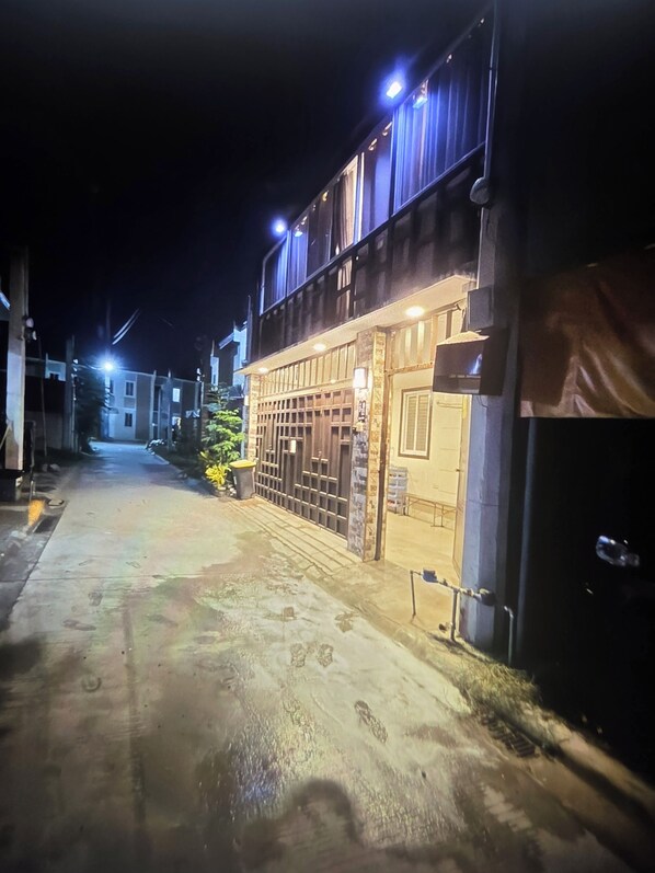 Vista nocturna de una calle con un edificio que tiene entrada porticada y ventanas iluminadas.