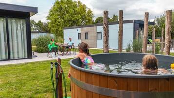 A wooden hot tub in a backyard with a modern house in the background.
