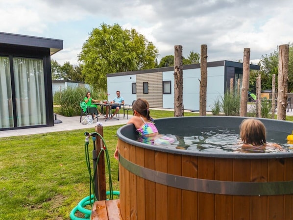 A wooden hot tub in a backyard with a modern house in the background. - Cube la Mer Wellness 4 (Warmond)