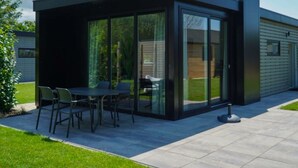 Un pati exterior modern amb tancament de vidre, una taula i caires, i un jardí.