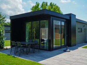A modern outdoor patio with a glass enclosure, a table with chairs, and a lawn. - Cube la Mer Wellness 4 (Warmond)