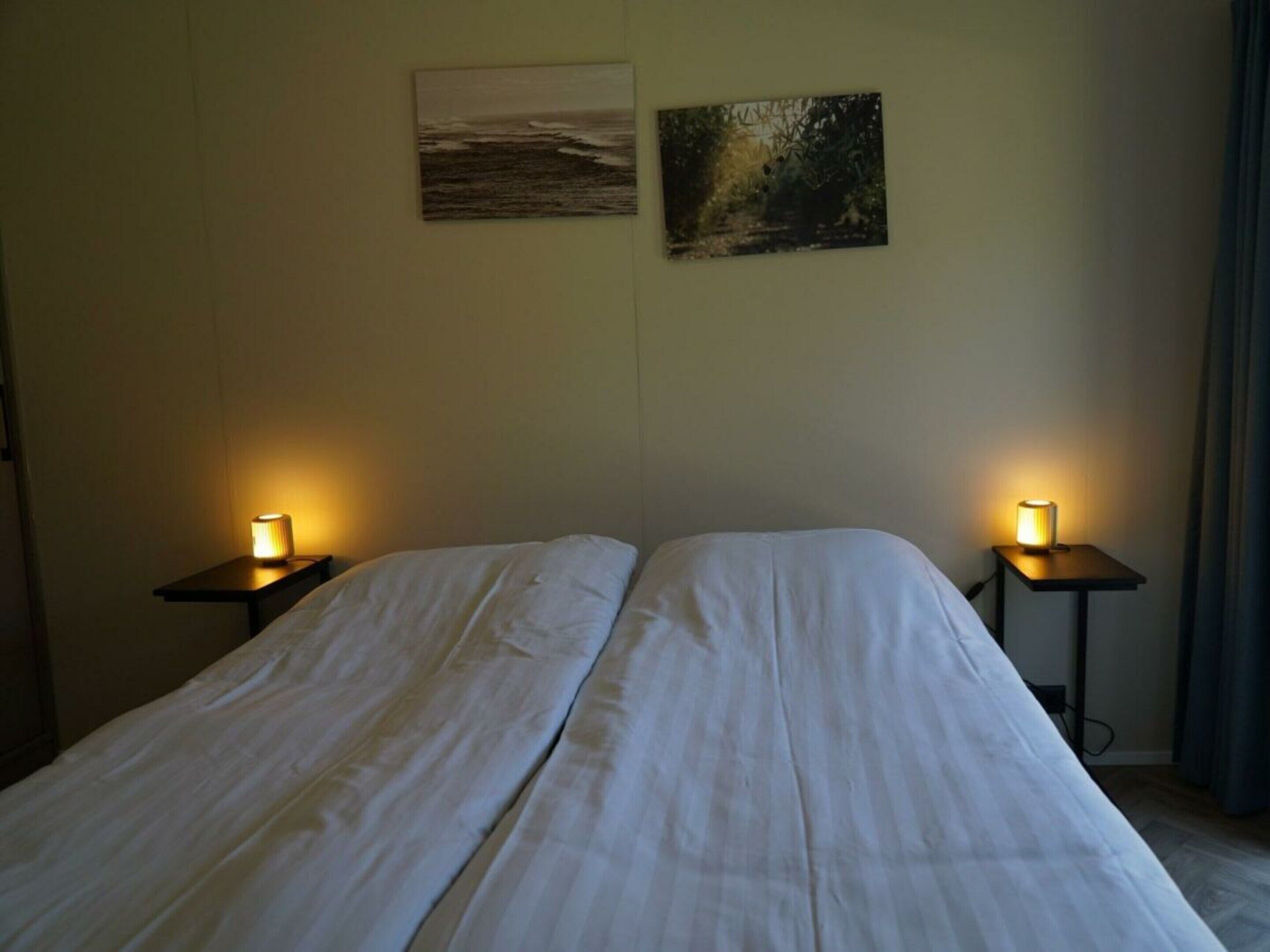 A hotel room with a bed, two bedside tables with lamps, and two wall-mounted paintings.