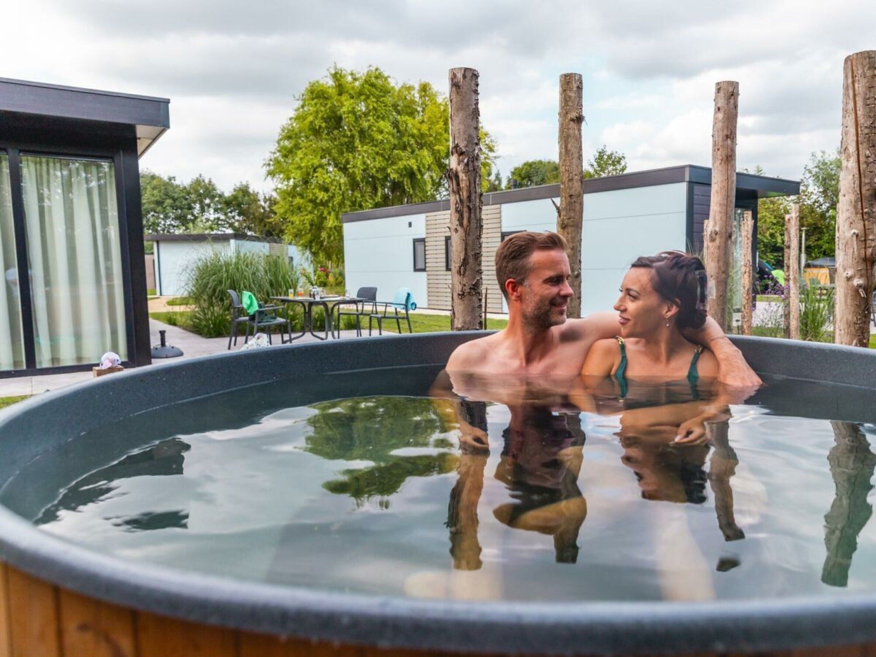 A couple in a hot tub with a modern building and outdoor furniture in the background.
