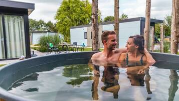 A couple in a hot tub with a modern building and outdoor furniture in the background.