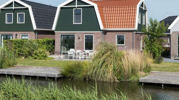 A row of modern houses with green and red roofs, a grassy area, and a body of water in the foreground. - Holiday Home in Uitdam With Terrace (Uitdam)
