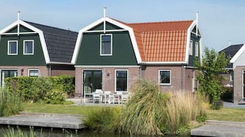 A row of modern houses with green and red roofs, a grassy area, and a body of water in the foreground.