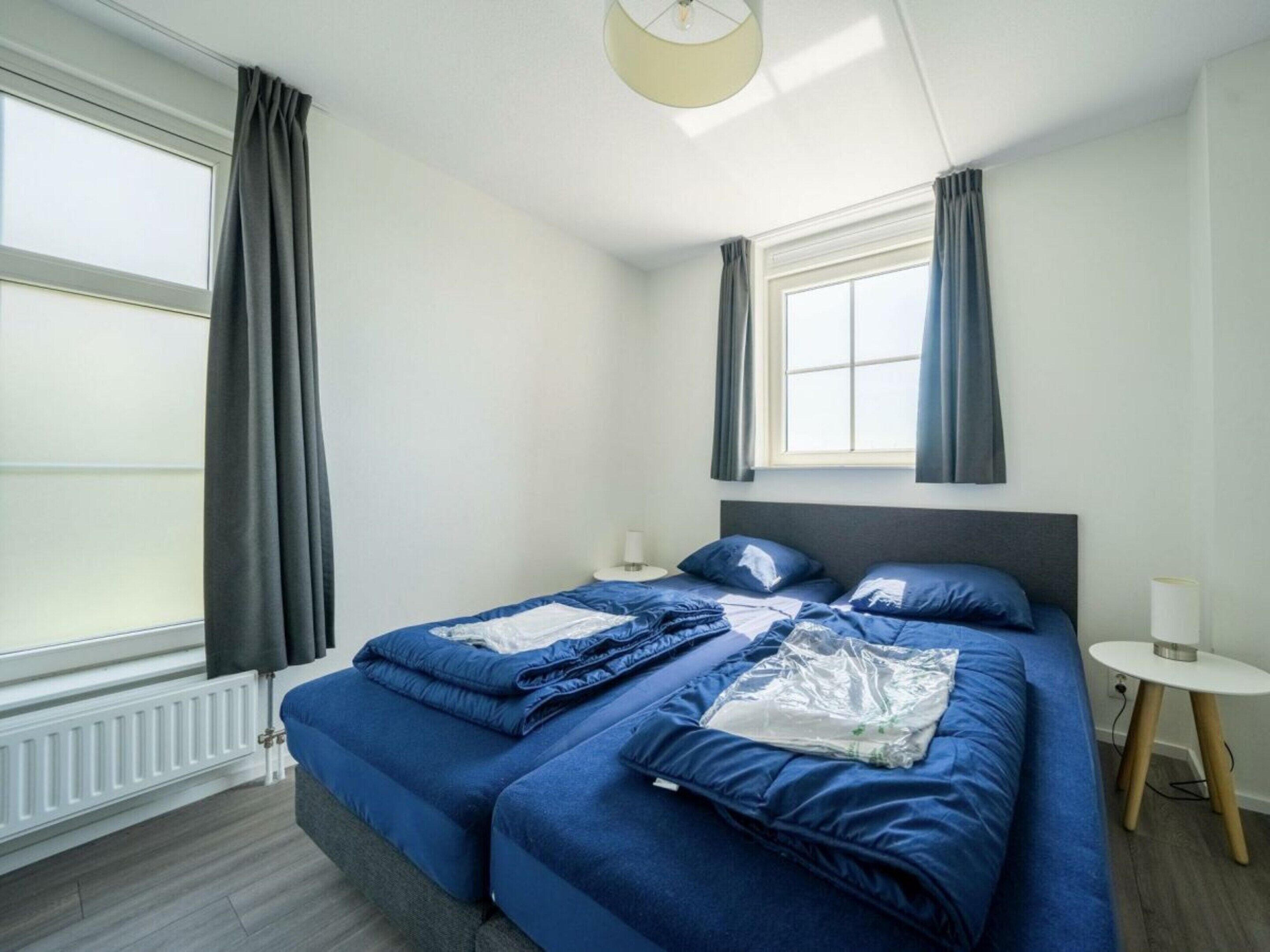 A room with a bed, a small table, a lamp, and a window with curtains.