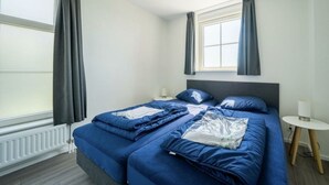A room with a bed, a small table, a lamp, and a window with curtains. - Holiday Home in Uitdam With Terrace (Uitdam)