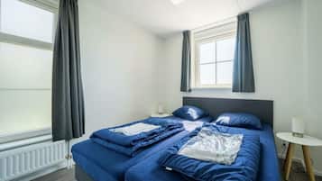A room with a bed, a small table, a lamp, and a window with curtains.