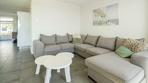 A modern living room with a sectional sofa, two white coffee tables, and a painting on the wall. - Holiday Home in Uitdam With Terrace (Uitdam)