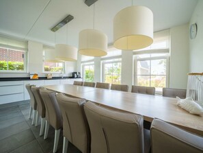 A modern kitchen with a long dining table, beige chairs, pendant lights, and large windows. - Holiday Home in Uitdam With Terrace (Uitdam)