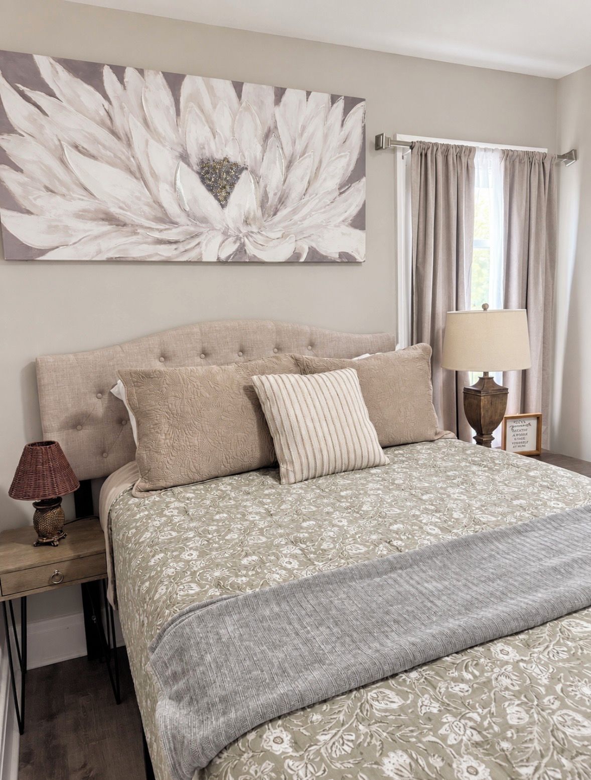 A bedroom with a large floral artwork on the wall, a bed with a patterned bedspread, and a bedside lamp.