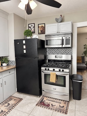 A kitchen with a black refrigerator, stainless steel microwave, and oven, with a farmhouse welcome mat.