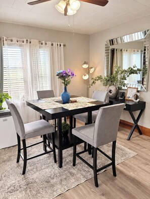 A dining area with a black table, four grey chairs, a blue vase with flowers, and a mirror on the wall.