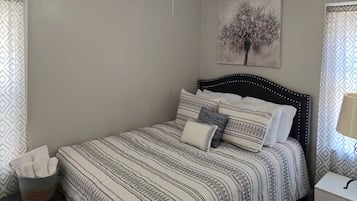 Une chambre à coucher comprenant un lit, un ventilateur de plafond, une table de chevet, une lampe et un mur orné d’un tableau encadré.
