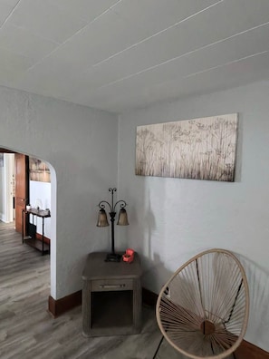 A hallway with a wooden floor, a small console table with a lamp, a chair, and a wall-mounted artwork.