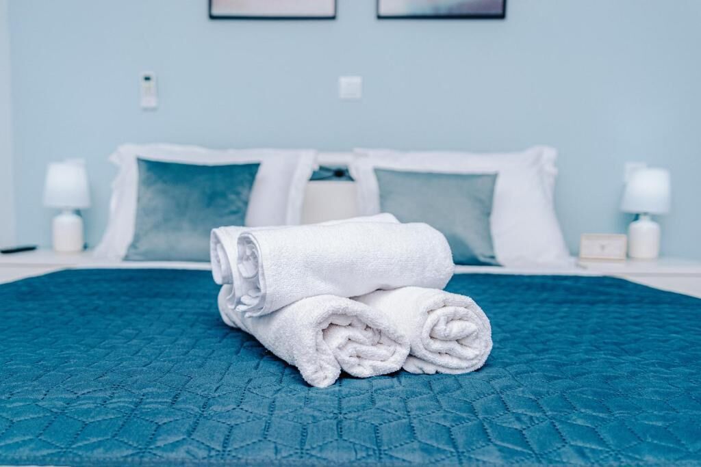 Una cama bien hecha con colcha azul, almohadas blancas y una toalla blanca enrollada sobre la cama.