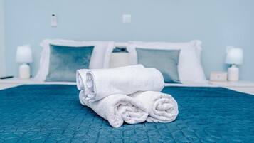 Una cama bien hecha con colcha azul, almohadas blancas y una toalla blanca enrollada sobre la cama.