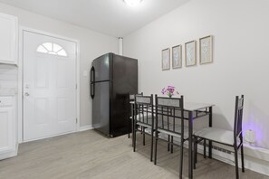 Eine Küche mit einem schwarzen Kühlschrank, weißen Schränken, einem Esstisch mit Stühlen und einer Wand mit gerahmten Blumenbildern.