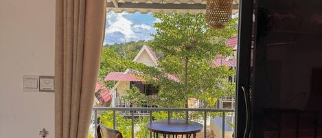 A balcony with a table and chairs, a hanging light fixture, and a view of houses and trees.