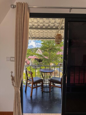 A balcony with a table and chairs, a hanging light fixture, and a view of houses and trees.