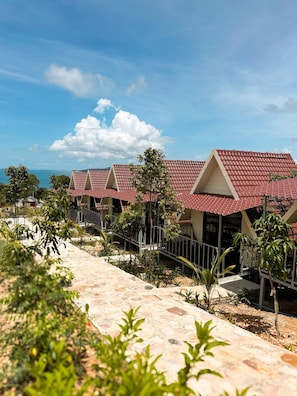 A row of red-roofed buildings with a stone pathway and greenery in the foreground.