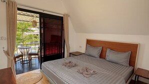 Un dormitorio con cama, cabecera de madera, una mesita, una silla y vistas a un espacio exterior con mesa y sillas.