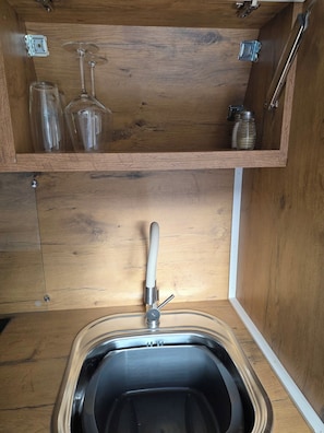 Un mueble de madera con un lavabo integrado, un grifo y una repisa con frascos de vidrio y una copa de vino.