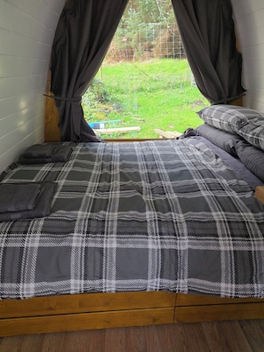 A bed with a plaid bedspread, a wooden headboard, and a window with curtains.