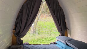 A small, cozy room with a bed, a wooden table, and a window with curtains.