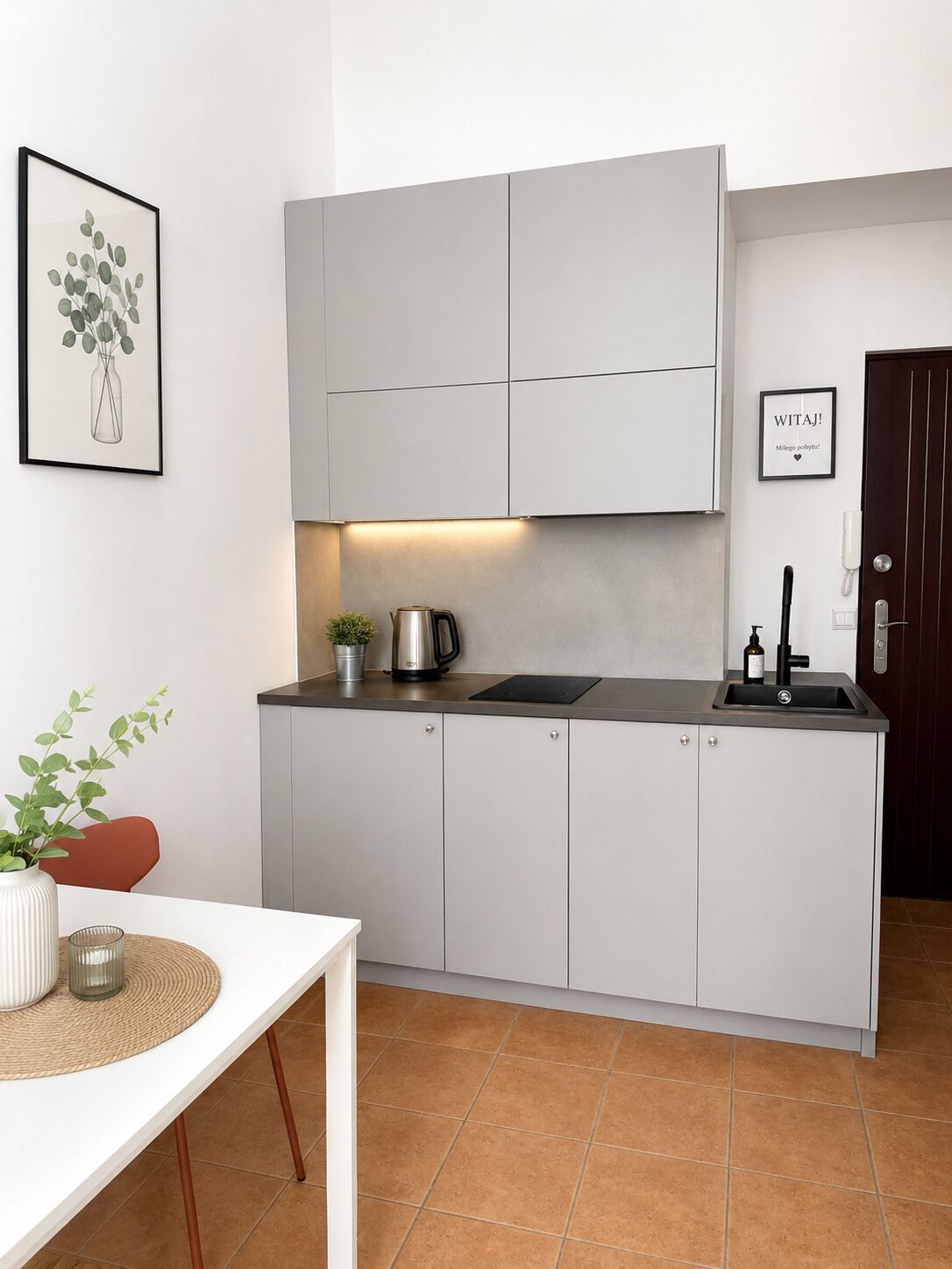 Una cocina moderna con armarios grises, una tetera, un lavamanos y un cuadro en la pared.