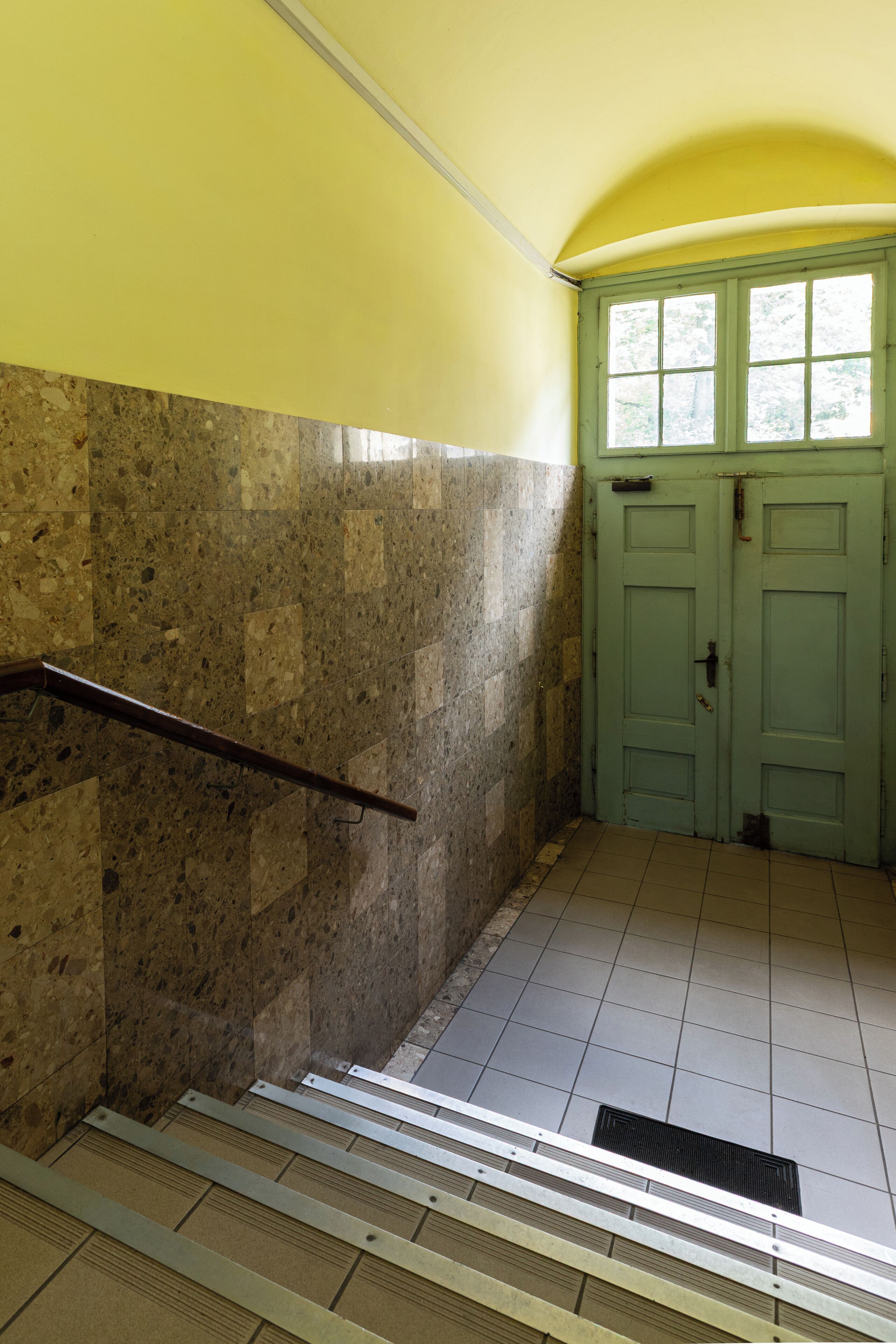 A stairway with metal handrails, a green door, and a tiled floor.