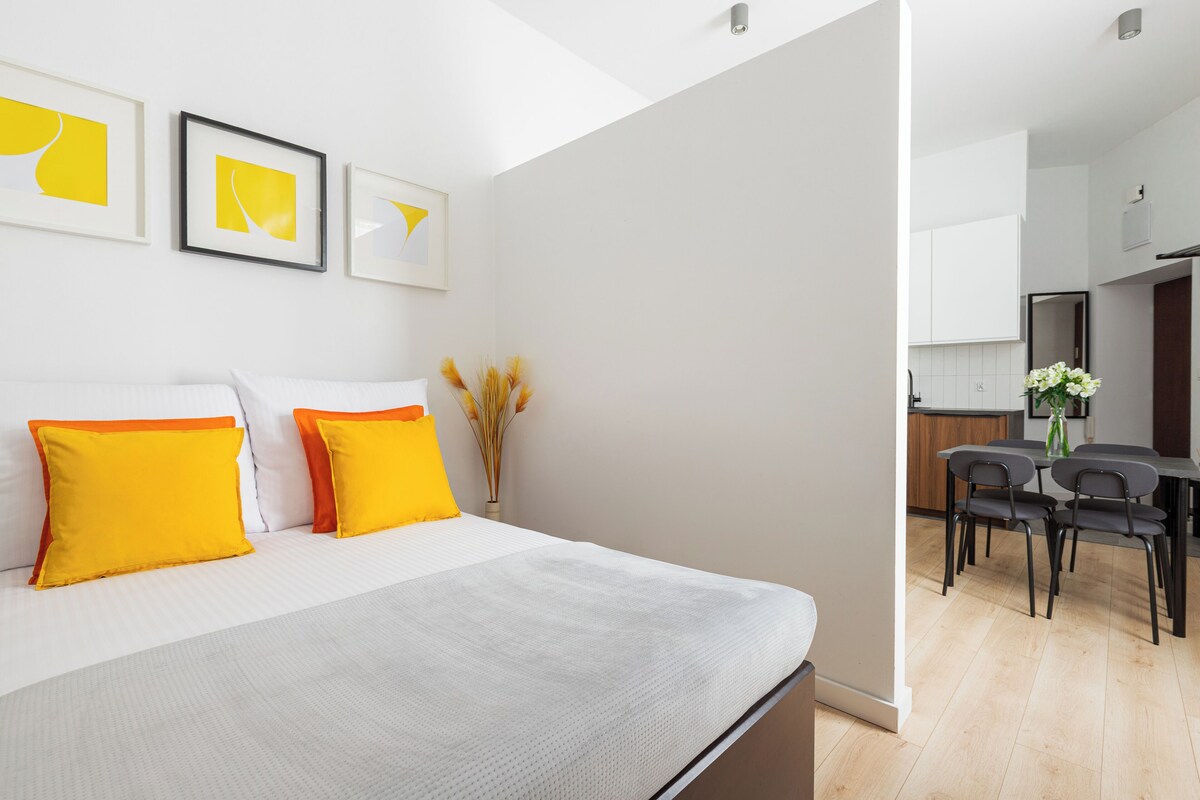 A modern bedroom with a bed, pillows, and a dining area with chairs and a table.