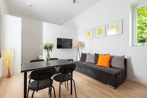 A modern living room with a sofa, a dining table with chairs, a flat-screen TV, and framed artwork on the wall. - Native Apartments Łazarza 3 (Kraków)