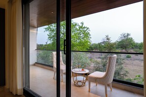 Un balcón con dos sillas, una mesa, una puerta de cristal y vistas a la vegetación.