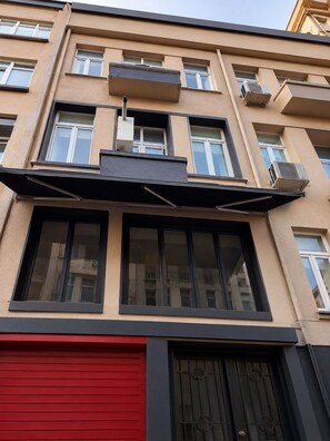 Um edifício com várias andares, varandas, janelas amplas e uma porta de garagem vermelha.