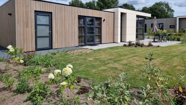 Un bâtiment moderne doté de grandes fenêtres, d’une façade en bois et d’une pelouse bien entretenue agrémentée de fleurs.