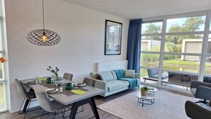 Un salon moderne avec un coin repas, de grandes fenêtres et une vue sur l’extérieur.